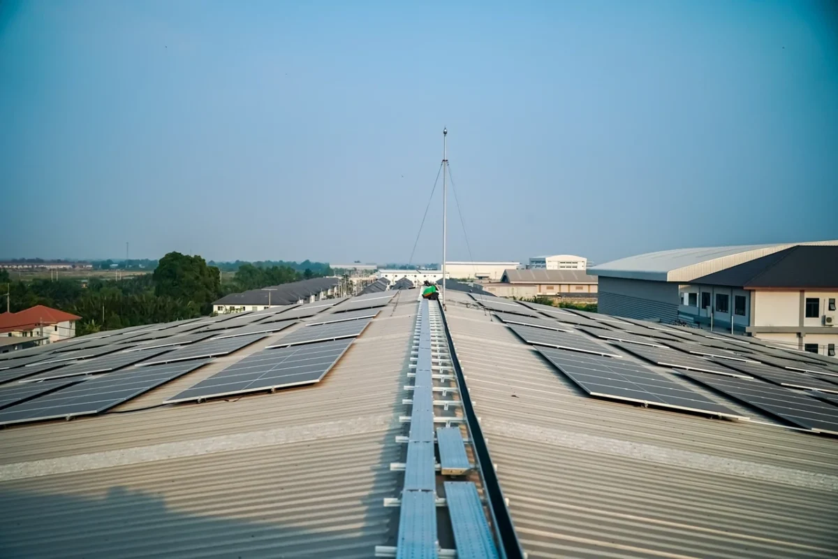 Tetto industriale con pannelli fotovoltaici e inverter ibridi in parallelo, con un tecnico che esegue la manutenzione.