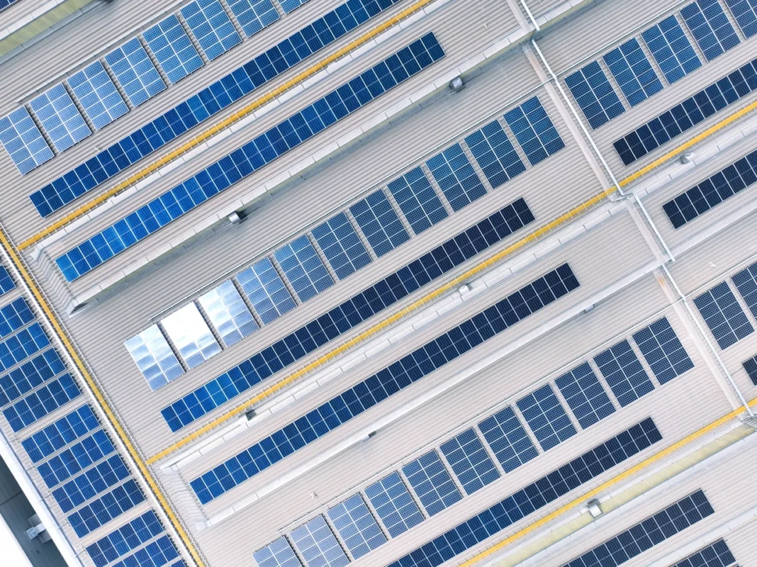 Veduta aerea di un impianto di pannelli solari sul tetto di un edificio industriale, utilizzato per la produzione di energia in loco al fine di ridurre i costi energetici e le emissioni di carbonio.