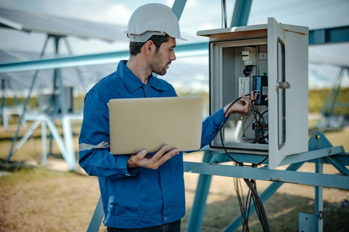Un tecnico connette un laptop a un quadro elettrico per la manutenzione predittiva di un impianto fotovoltaico.
