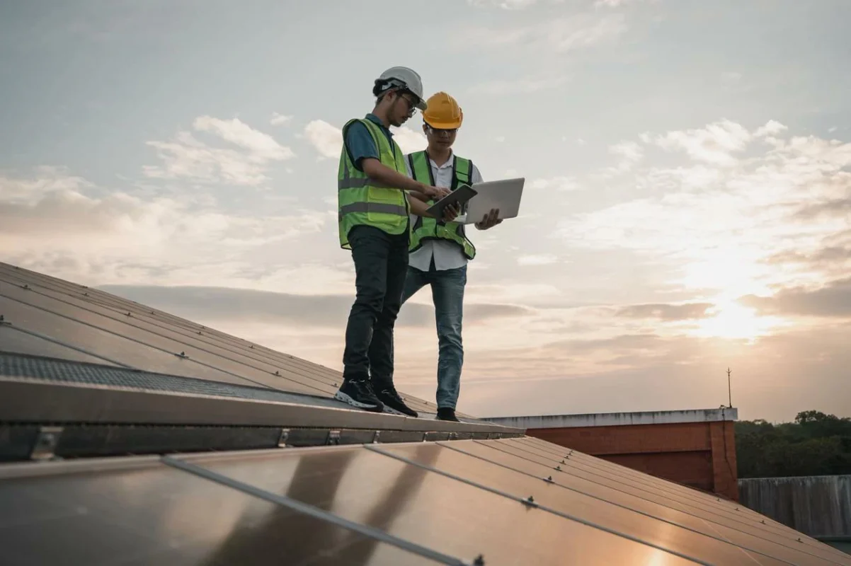 Ingegneri certificati analizzano i dati su laptop sul tetto, ottimizzando le prestazioni dell'impianto fotovoltaico.