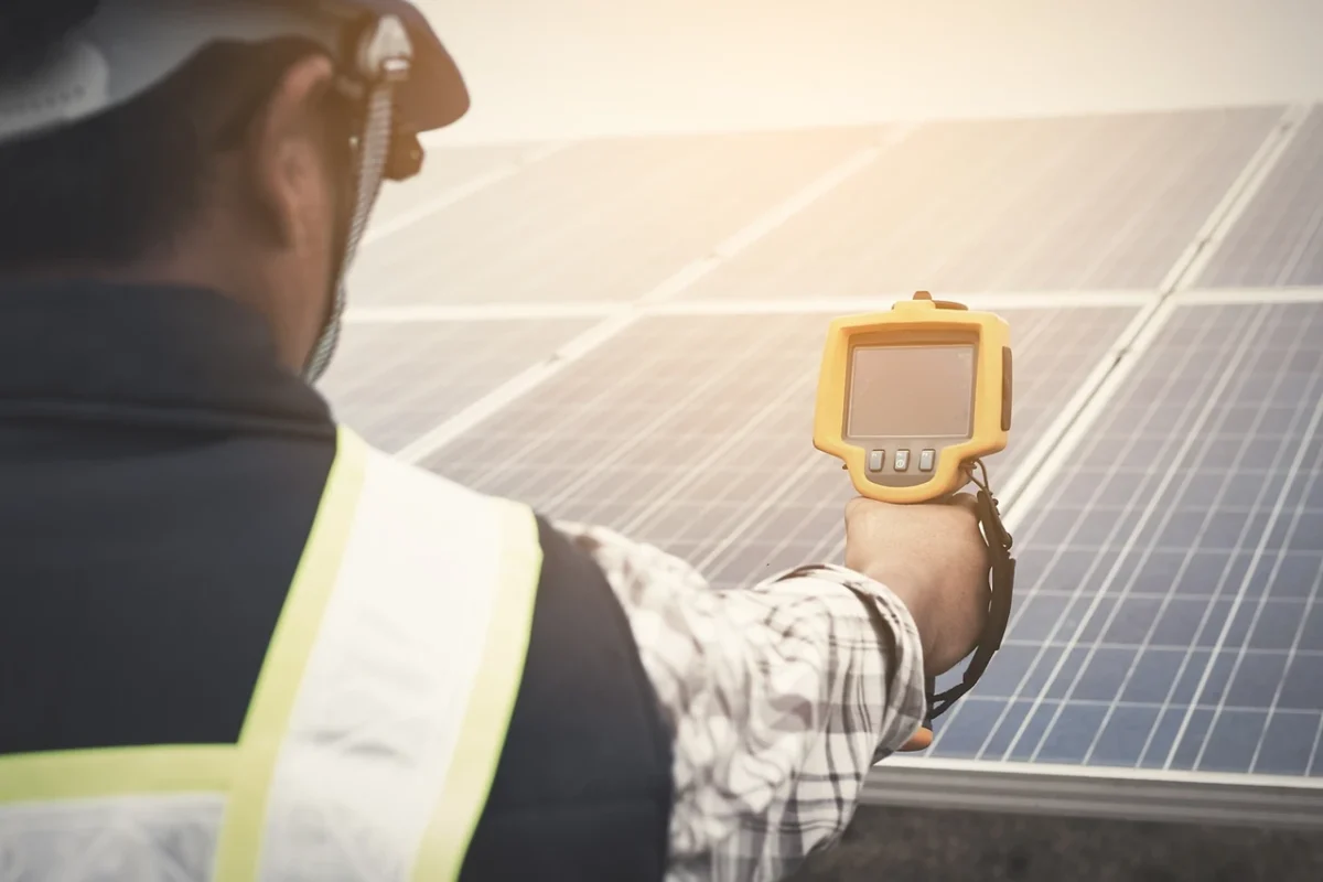 Tecnico che utilizza una termocamera per rilevare difetti nei pannelli fotovoltaici durante un audit DNSH.