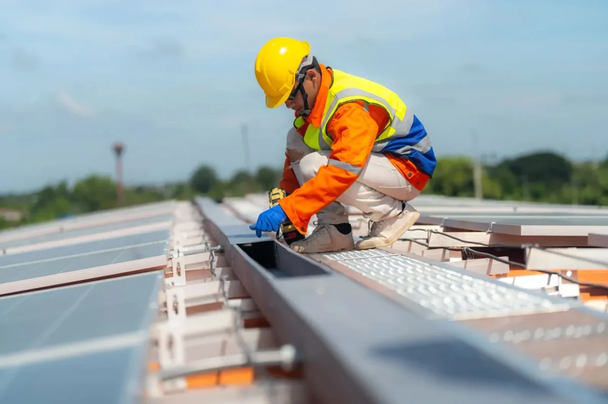 Operatore specializzato in sicurezza installa e fissa componenti di un impianto fotovoltaico industriale sul tetto di un capannone italiano.