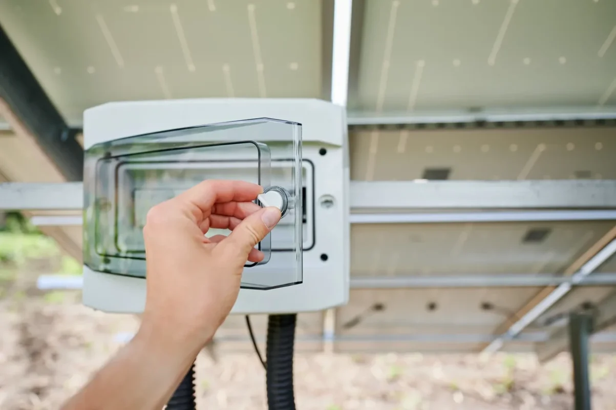 Mano regola l'interruttore di un inverter fotovoltaico, mostrando le operazioni di manutenzione per risolvere guasti.