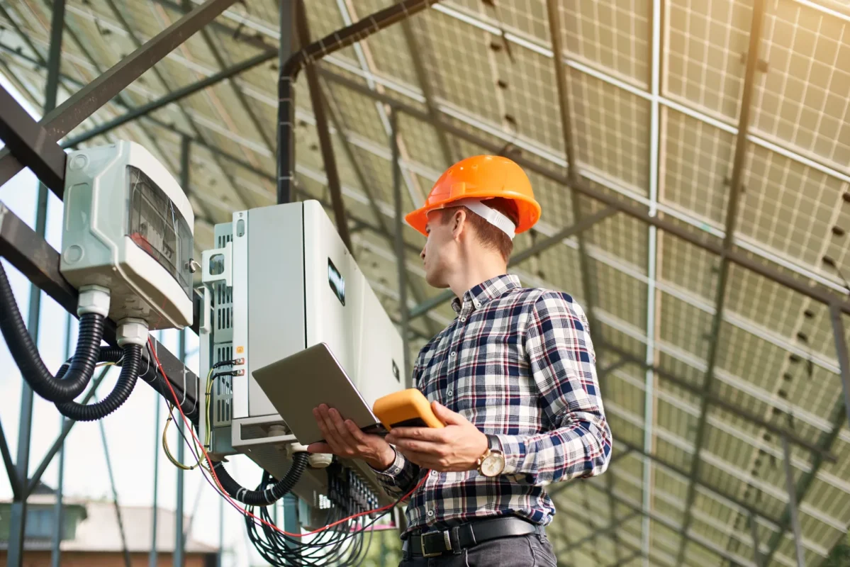Tecnico con elmetto e laptop che verifica l'inverter di un impianto fotovoltaico.
