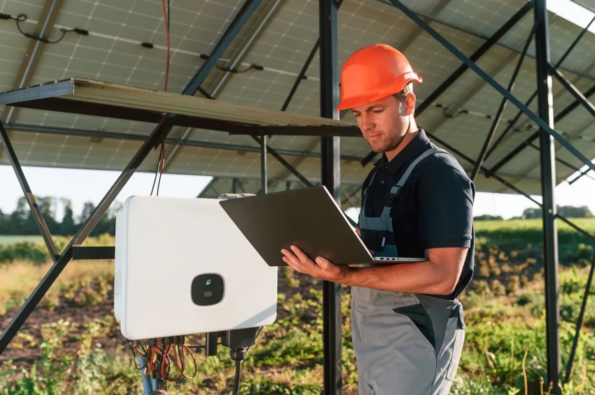 Tecnico verifica un inverter fotovoltaico IP66 con un laptop, controllando le prestazioni in ambienti esterni.