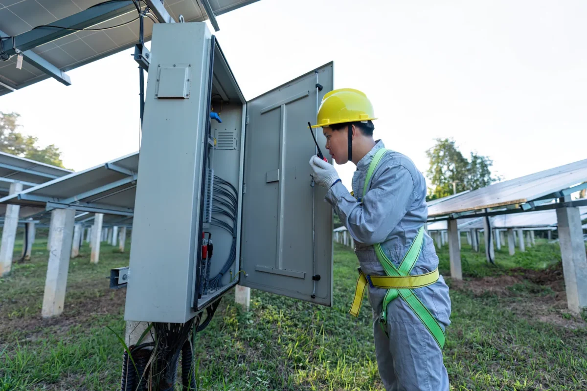 Tecnico che controlla un quadro elettrico di un impianto fotovoltaico vicino ai pannelli solari.