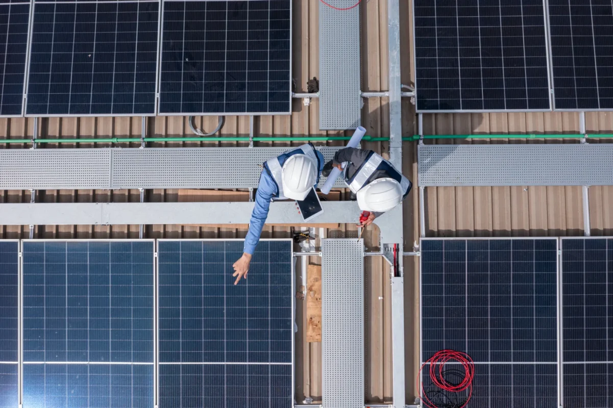 Vista dall’alto di tecnici che controllano pannelli fotovoltaici per impianti con inverter ibrido o on-grid tradizionale.