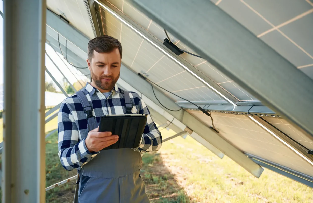 Tecnico verifica produzione impianto fotovoltaico con tablet su pannelli solari esterni.