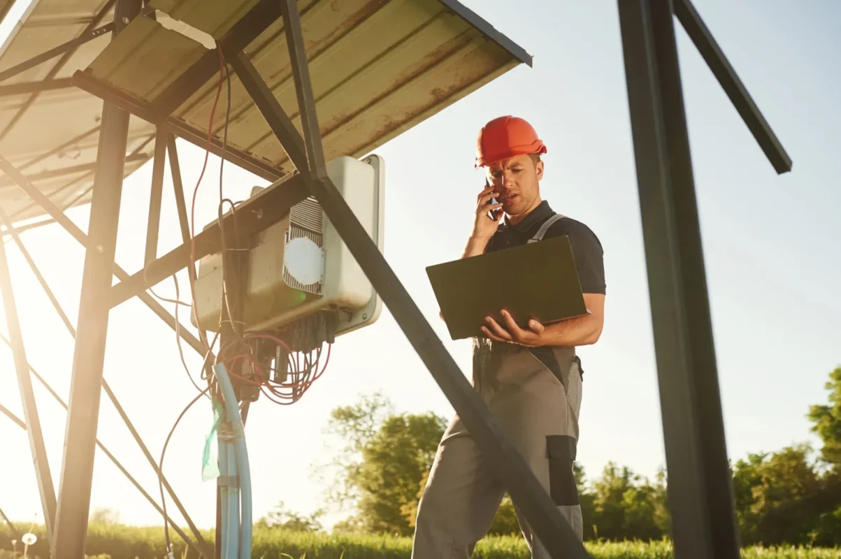 Operatore usa laptop e telefono per controllare l’inverter di un impianto solare da remoto.