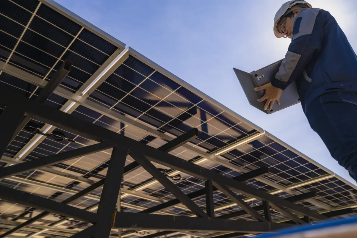 Técnico inspecionando painéis solares em um complexo de habitação multifamiliar, utilizando um laptop para o monitoramento de um projeto B2B.