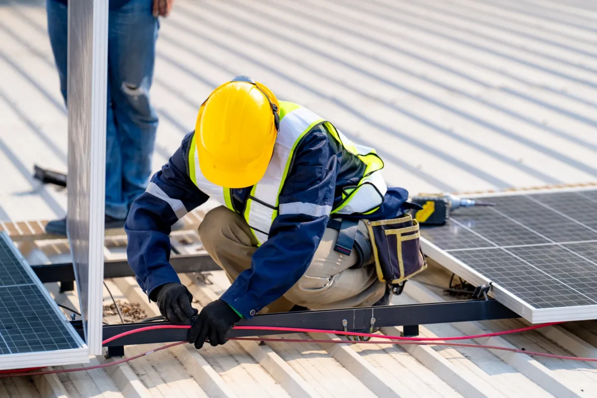 Technician installing solar panel wiring on a commercial rooftop, part of EPC-financed solar projects.