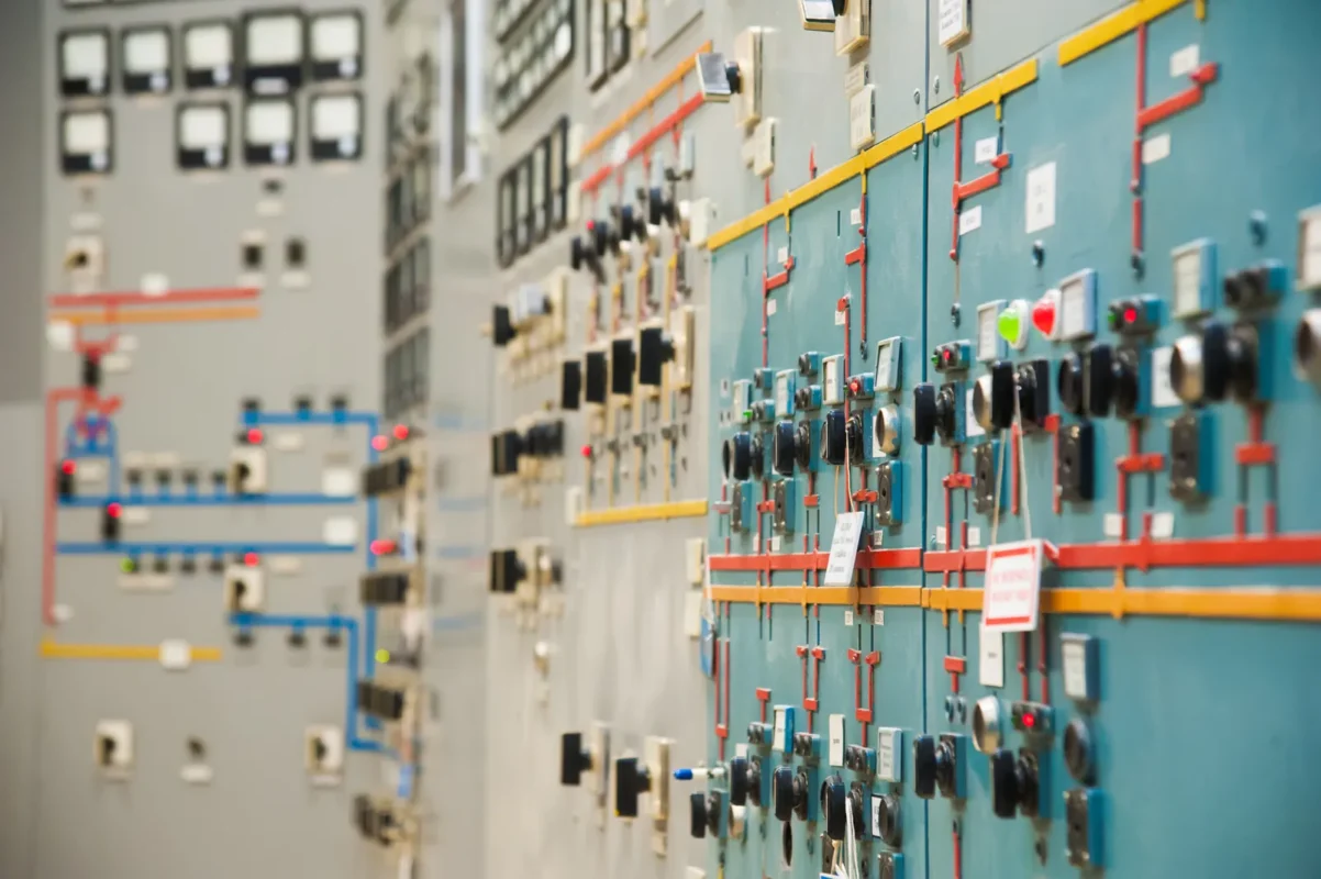 Wide shot of industrial electrical control panel lined with switches, indicator lights and colored wiring for off-grid inverter power system management.