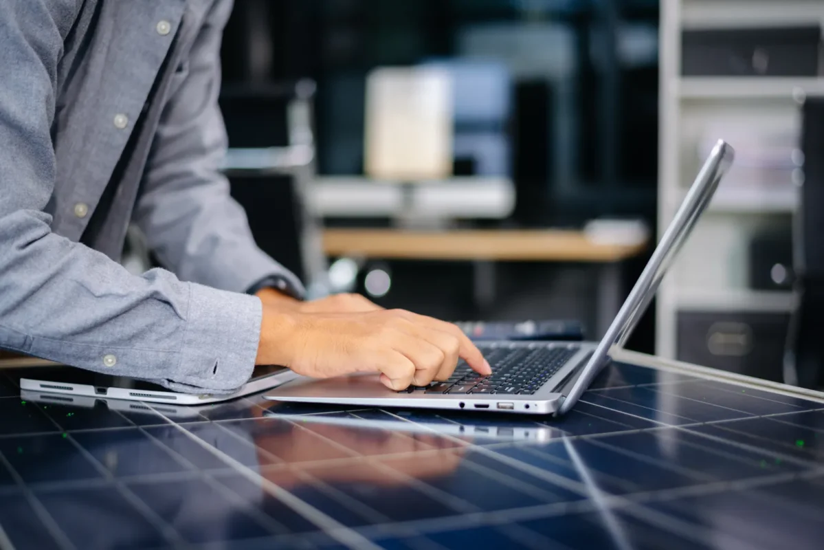Person working on a laptop, likely managing or scheduling solar inverter replacement services.