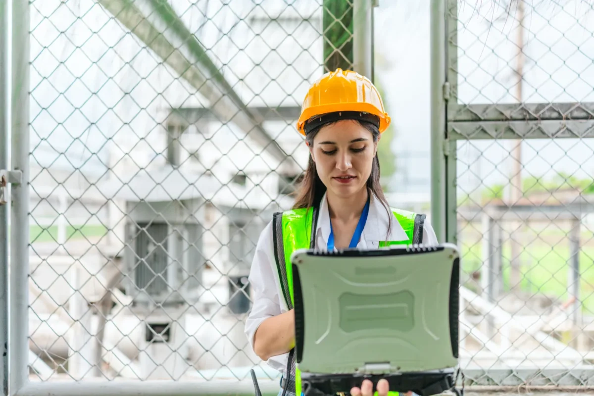 Professional facility engineer using rugged industrial laptop to monitor and adjust parameters of commercial hybrid inverter solar battery storage systems remotely.