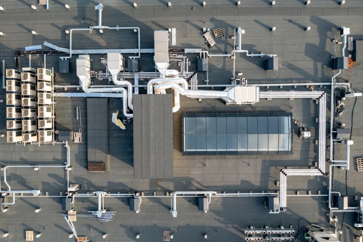 Top-down aerial shot of industrial building rooftop with HVAC piping, air conditioning units and reserved space for commercial solar system installation design.