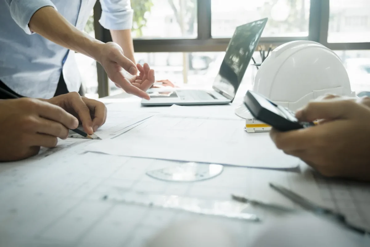 EPC engineering team calculating solar inverter efficiency metrics, lifecycle costs and LCOE on construction blueprints for commercial PV project procurement comparison.